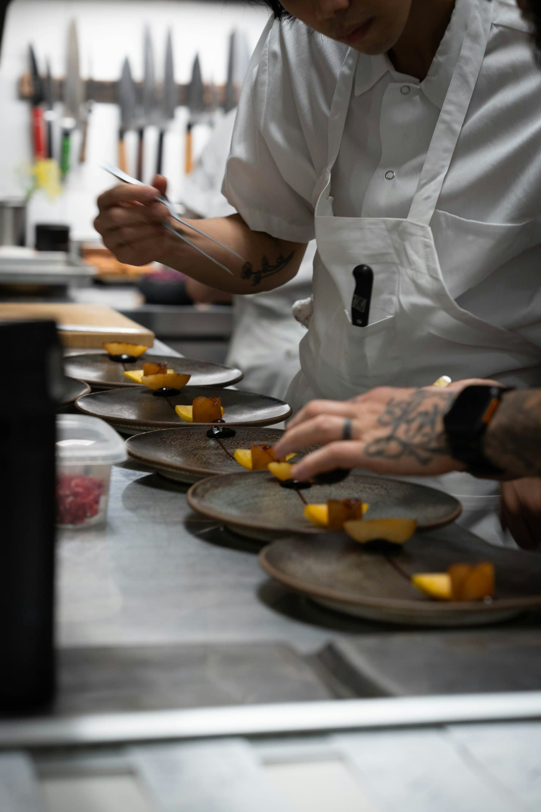 A cook plating several identical portions along a kitchen pass.